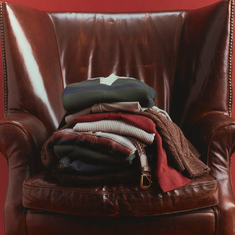 A stack of folded clothing and a brown leather armchair against a solid red background.