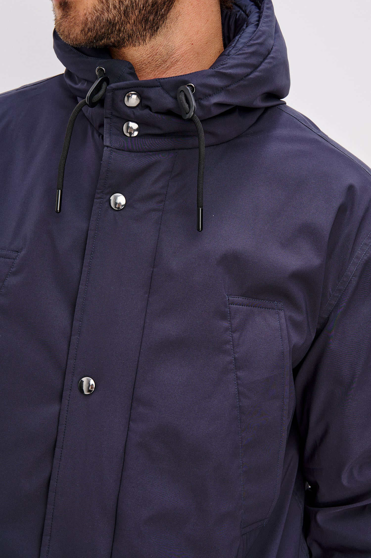 Rainier is a hooded parka coat, water-resistant and features hand warming pockets with snap closure, drawcord at hood and waist for sinching effect and a double flap center front closure and back seam vent in Navy colorway. Front detailed view featured on model.
