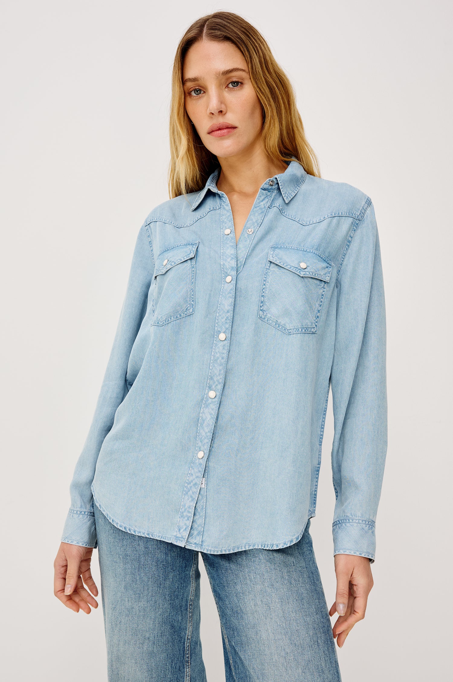 Remi is a utility-style Tencel denim shirt with a relaxed fit. The shirt features a notched collar, two front flap pockets, and faux horn buttons etched with a logo in medium indigo colorway - Front View Featured on Model