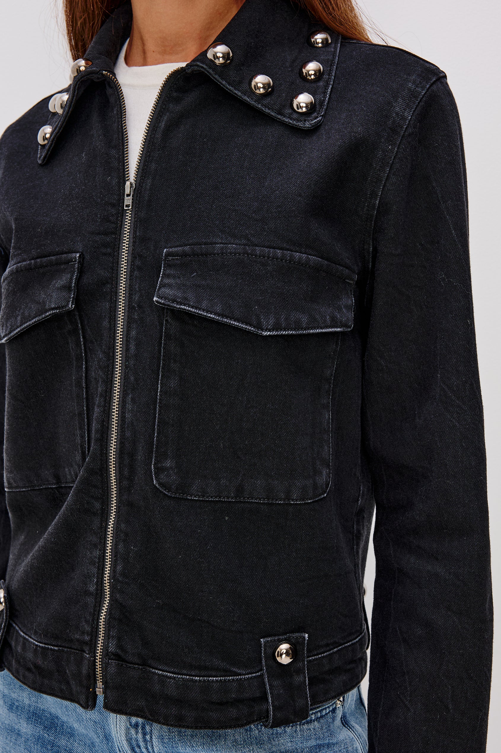 Roxbury Jacket in Denim With Boxy Fit, Nail-Back Studs at Oversized Collar, Long Sleeve Cuffs, and Hem, Oversized Chest Pockets With Hidden Snap Closures, Hem Tabs, and Front Zip in Black Stone Studded Colorway - Upper Body Front Close Up View Featured on Model