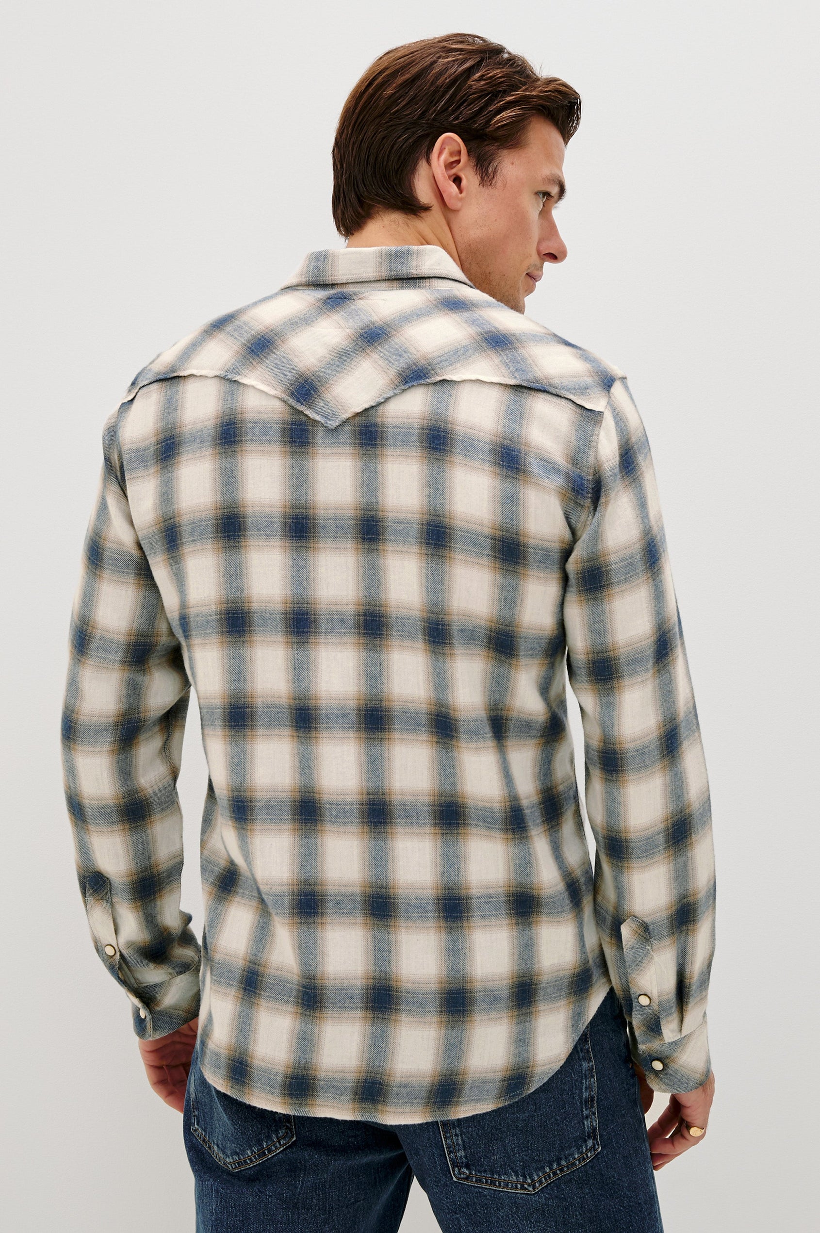 The Roy is a collared snap front shirt with long sleeves, two chest pockets, high low hem and a western yoke seam, in a plaid Wheat Marine Heather colorway. Back view featured on model.