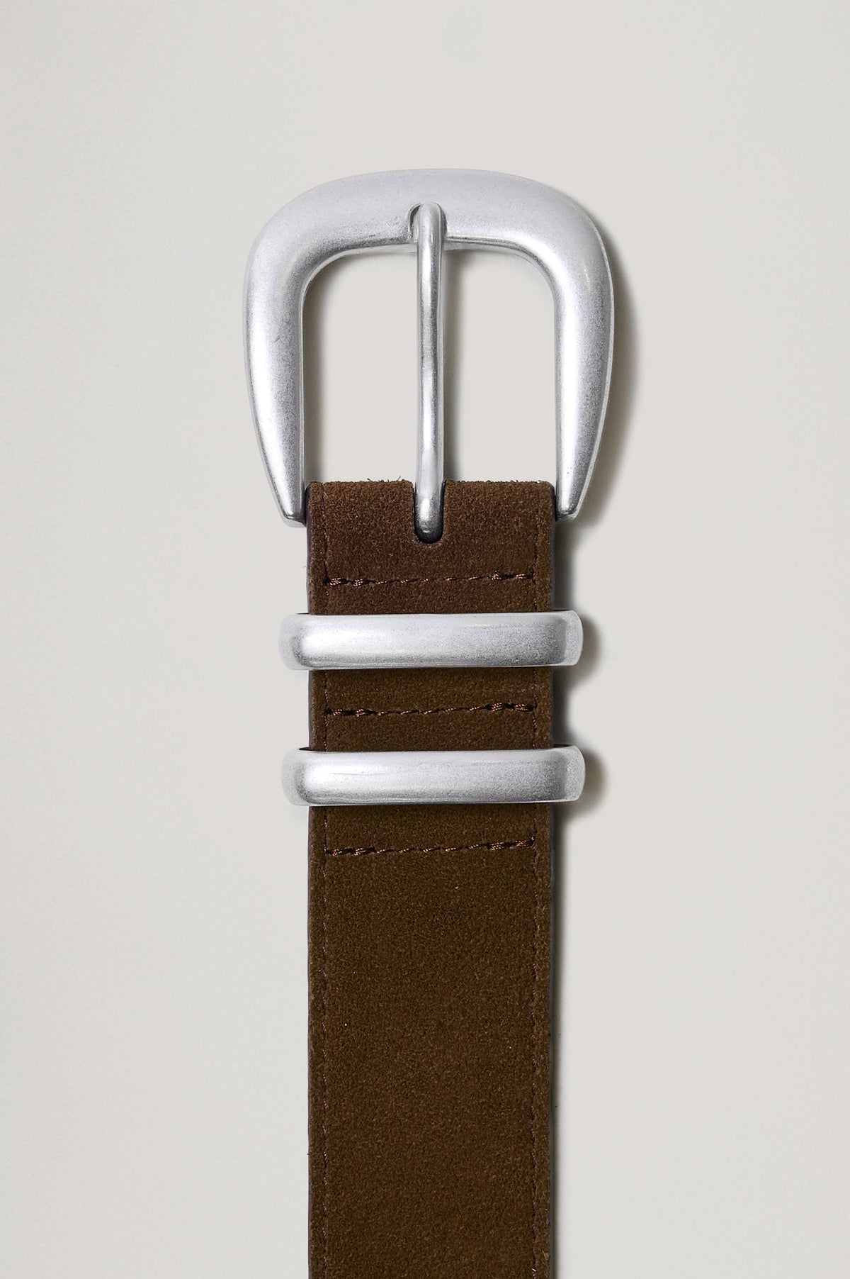Ryder suede leather belt features silver metal hardware, a metal tip in Chocolate colorway, flat front close up view of buckle featured 