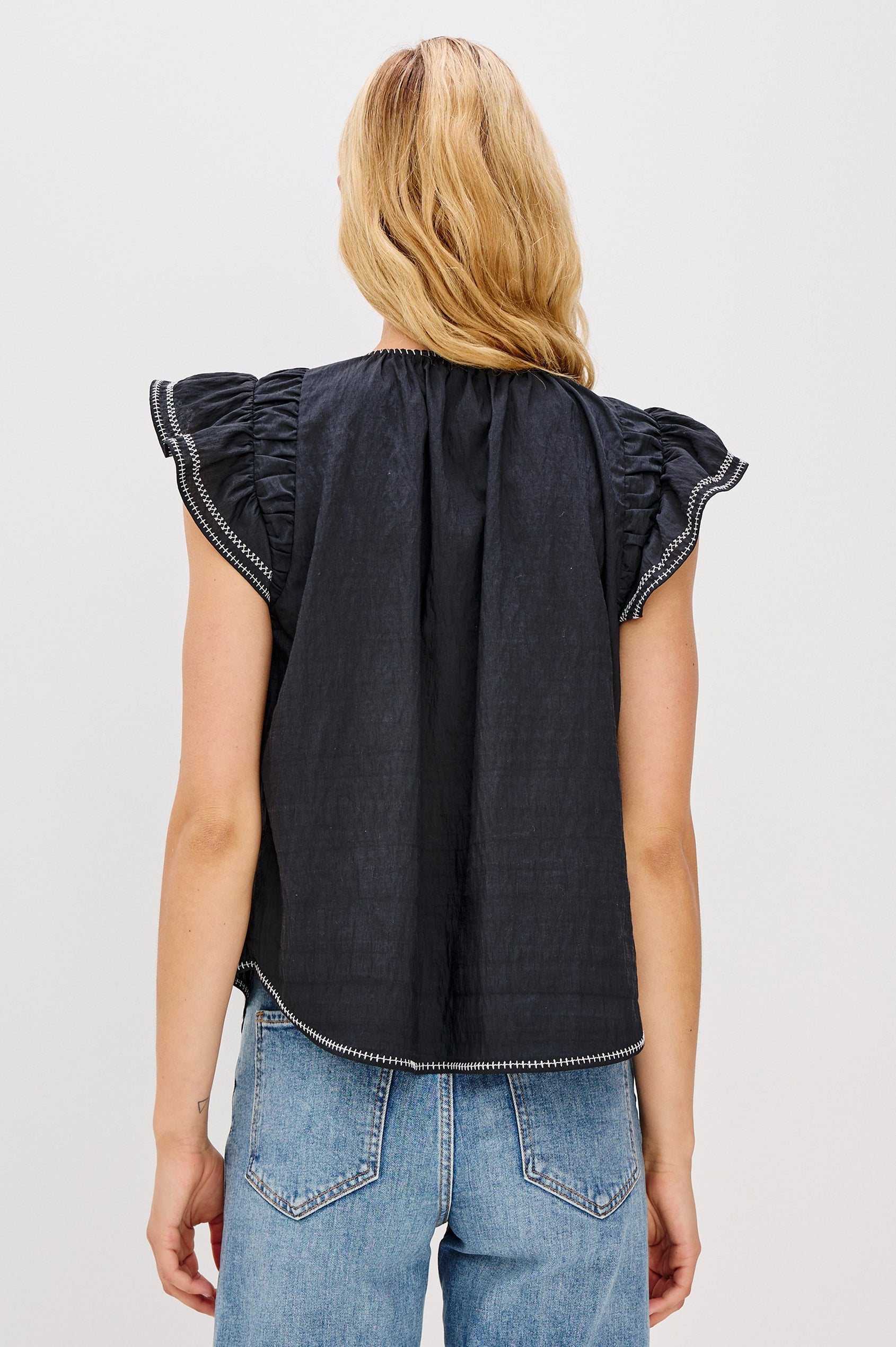 Sable is a scoop neck top with flutter sleeves and a split neck that is adjustable with a button, it has a high low hem and contrast white stitching in Black colorway. Back view featured on model.