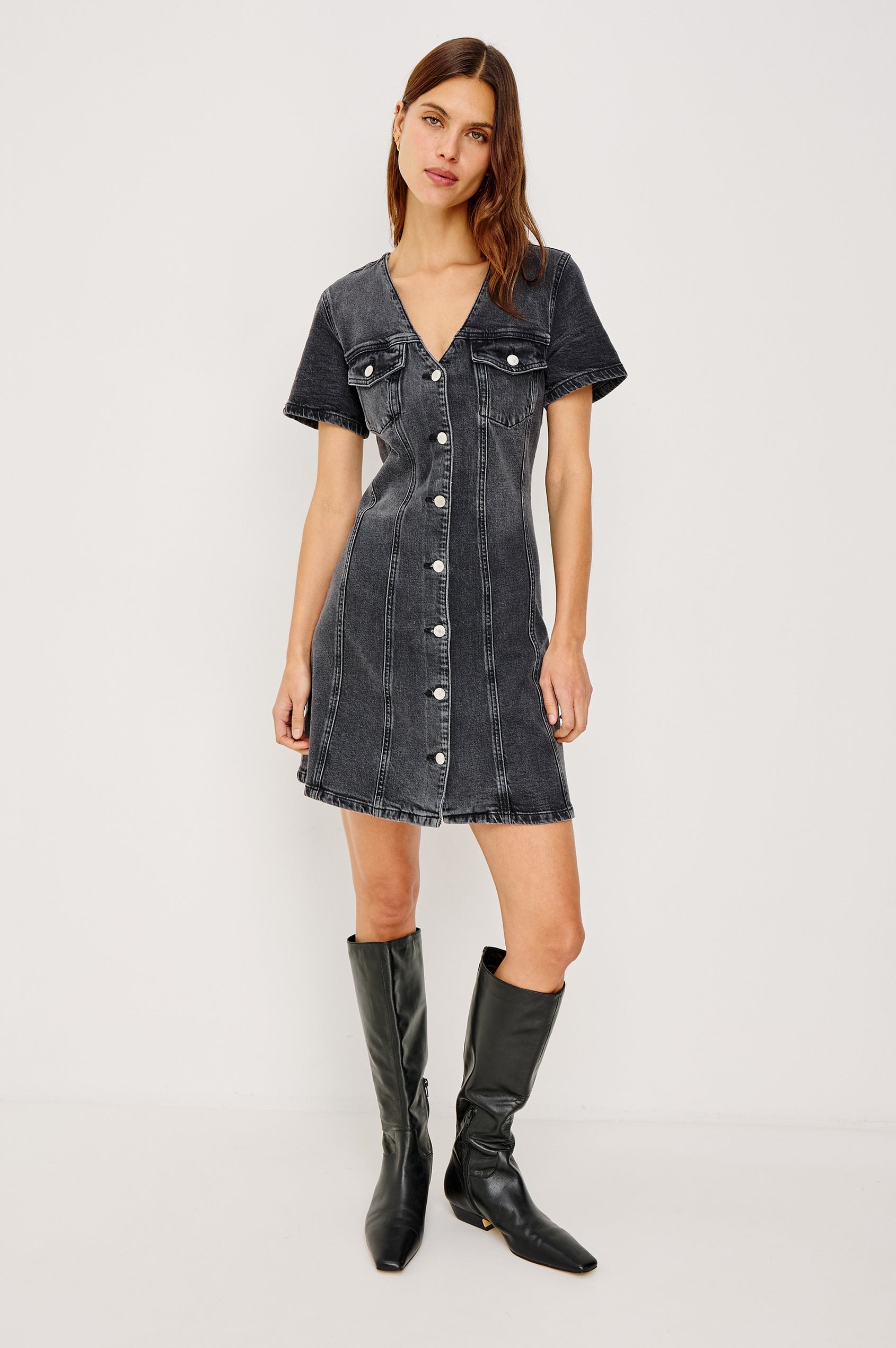 Saratoga Denim Mini Dress With V-Neckline, Buttoned Chest Pockets and Front Buttons, Short Sleeves, Seam Details, and A-Line Silhouette in Washed Black Colorway - Full Body Front View Featured on Model