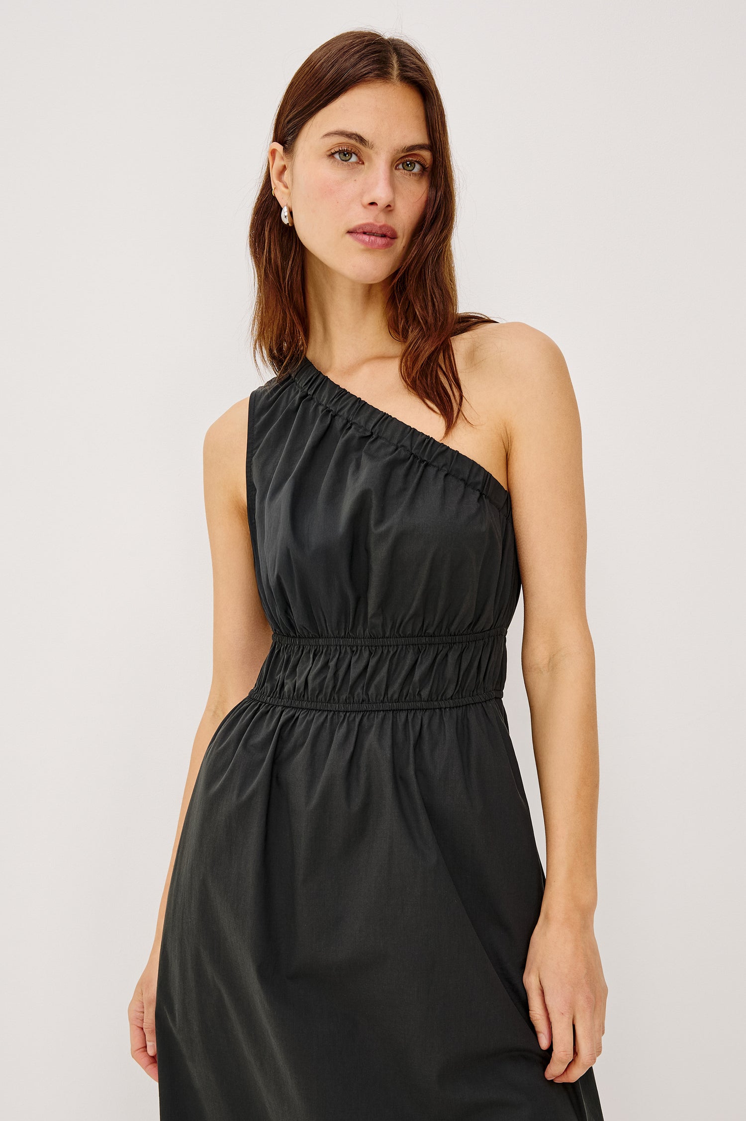 Selani Midi Dress With an Asymmetrical Neckline, Mid-Thigh Slide Slit and Cinched Waistband in Black Colorway - Front Full Body View Featured on Model