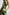 Selani Midi Dress With an Asymmetrical Neckline, Mid-Thigh Slide Slit and Cinched Waistband in Plumerias Colorway, with Ivory and Gold Plumerias on Dark Green  - Side View Featured on Model