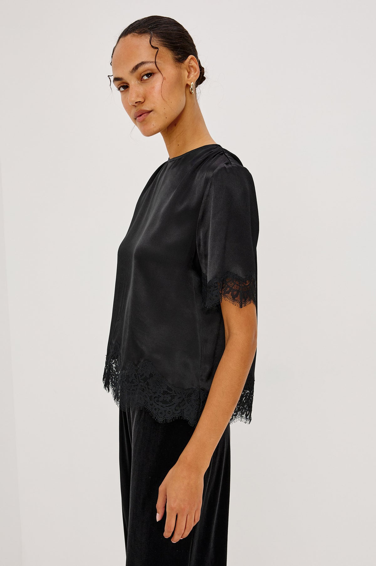 Sonora Shirt in Satin Crepe With Crew Neckline, Loose Boxy Fit, Shirred Shoulders, Short Sleeves, Button-Loop Back Keyhole, and Lace Trim in Black Colorway - Upper Body Side View Featured on Model