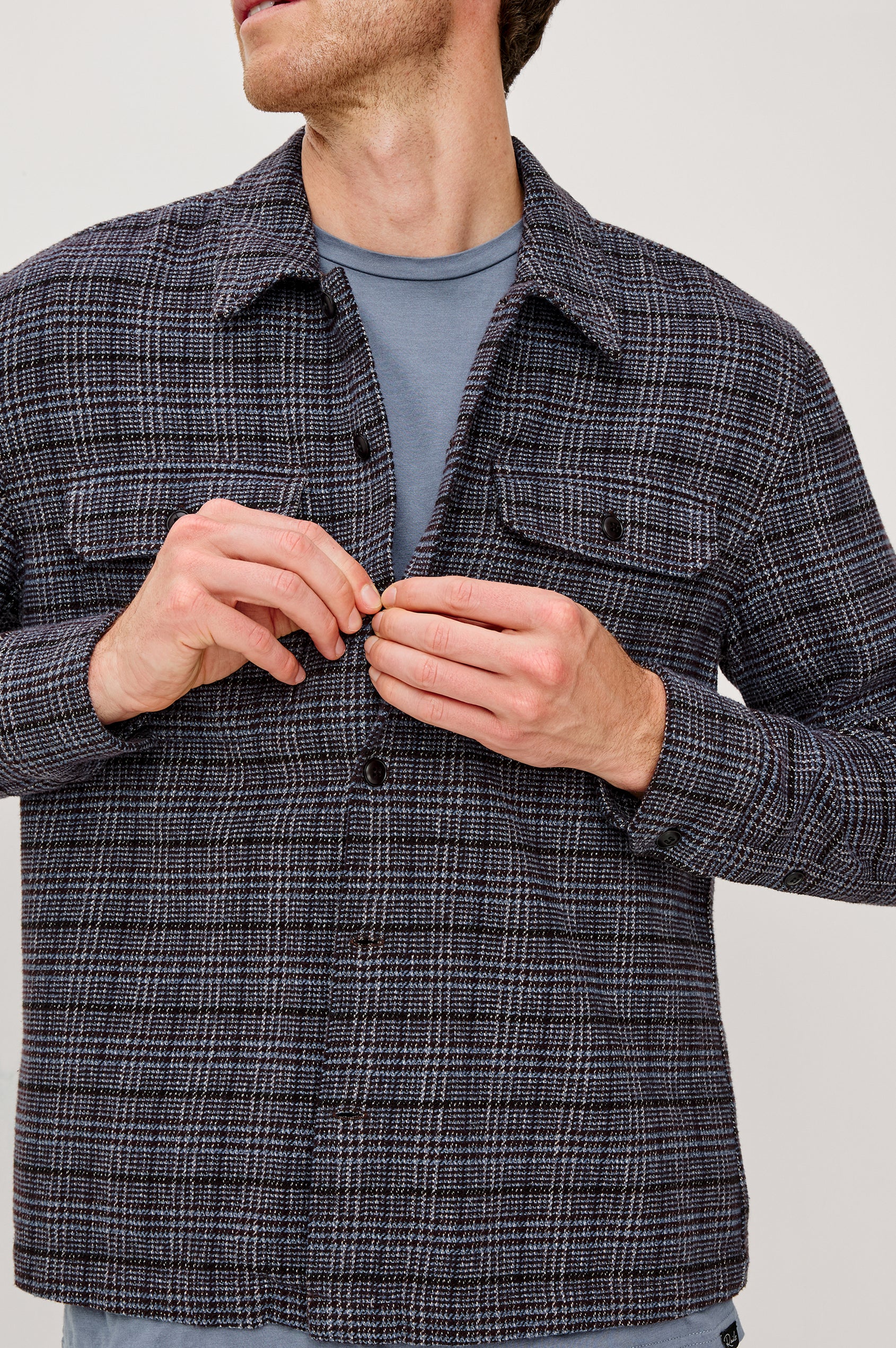 Stellan is a shirt jacket made from heavy brushed cotton with a classic collar, front button closures, chest flap pockets in Cedar Bay, a blue and grey plaid colorway. Front detail view featured on model.