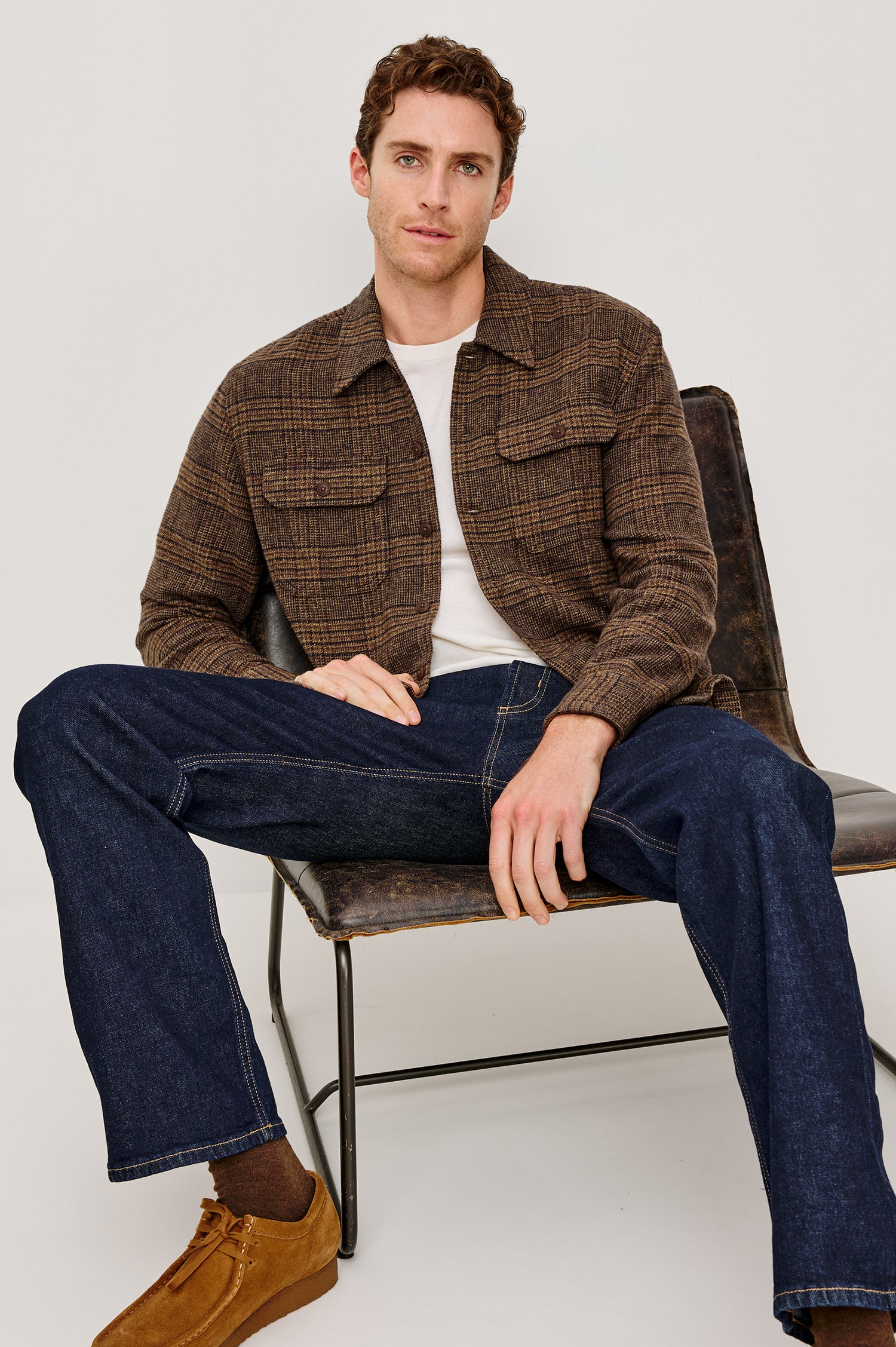 Stellan is a shirt jacket made from heavy brushed cotton with a classic collar, front button closures, chest flap pockets in Cedar Bay, a blue and grey plaid colorway. Front seated view featured on model.