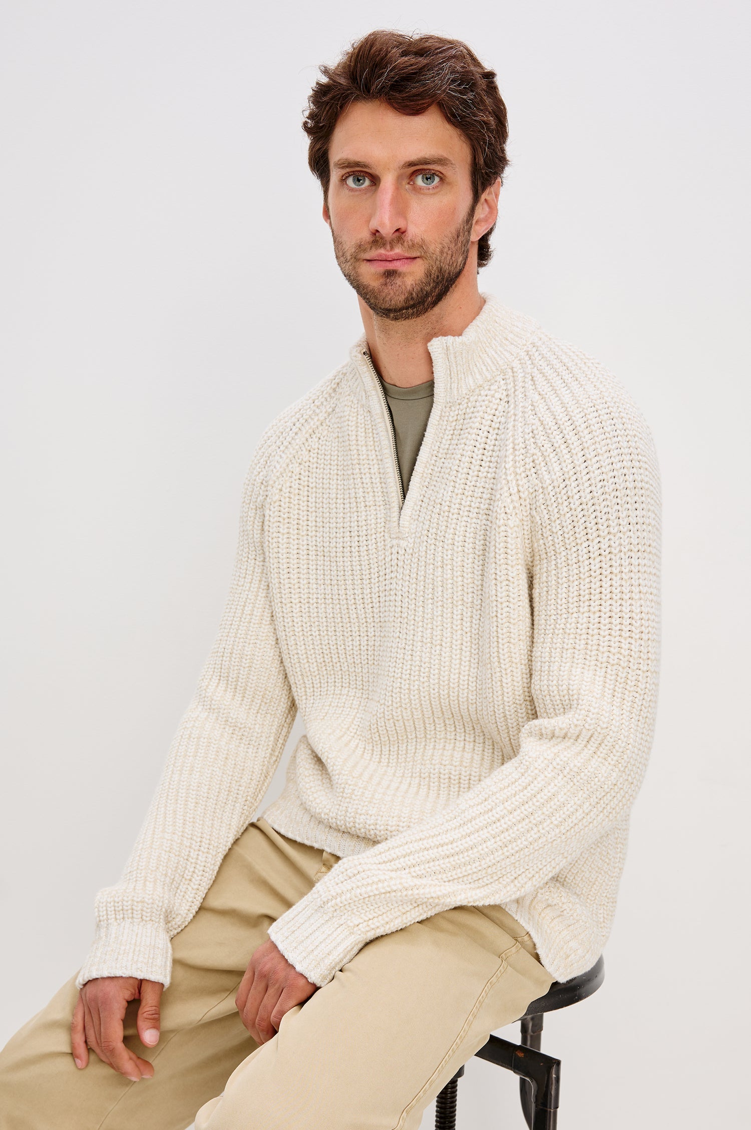 Stratton is a quarter-zip long sleeved sweater knitted from chunky cotton blend knit in Snowdrift Marl colorway. Front seated view featured on model.