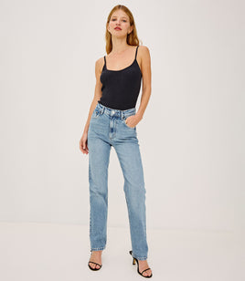 Woman wearing a black tank top and light blue jeans on a white background