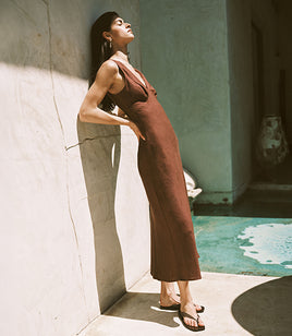 Woman in a brown dress leaning against a wall with a pool in the background
