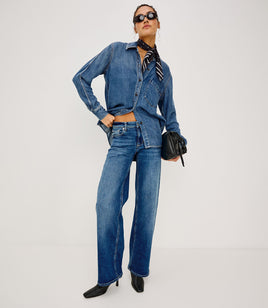 Person wearing a blue denim outfit with sunglasses and a black handbag on a white background