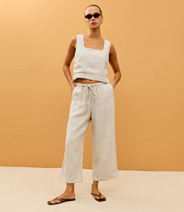 Woman wearing a white sleeveless top and light-colored pants against a beige background