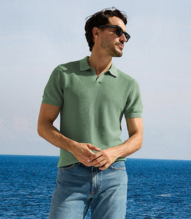 Man wearing a green polo shirt and sunglasses standing by the ocean.