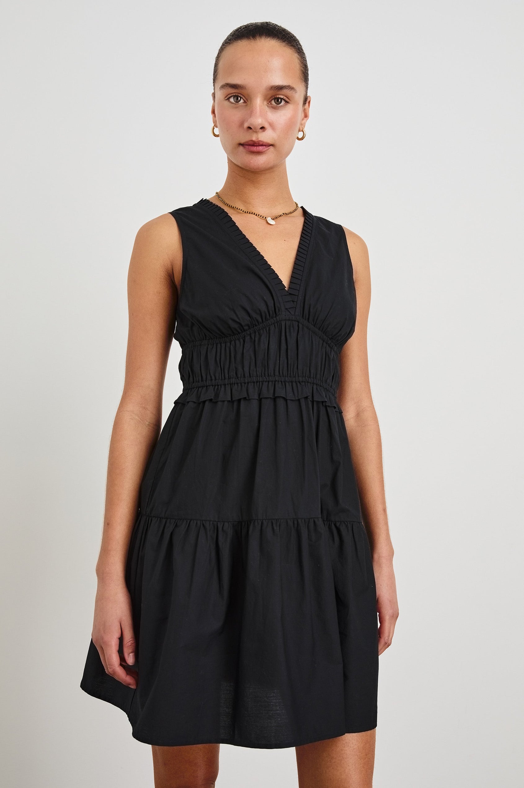 Front view of female model wearing our sleeveless, Talulah Mini Dress in color Black. Dress features pleated v-neck and smocked waist.
