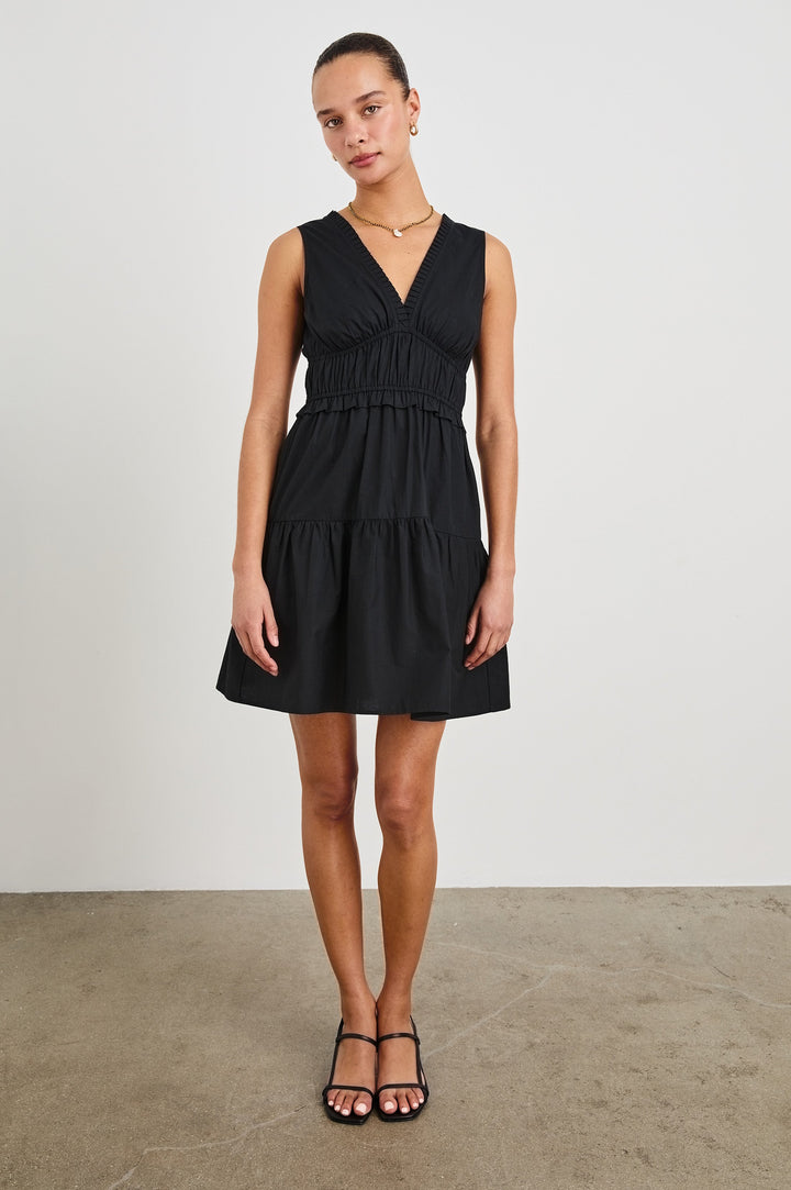 Front view of female model wearing our sleeveless, Talulah Mini Dress in color Black. Dress features pleated v-neck and smocked waist.