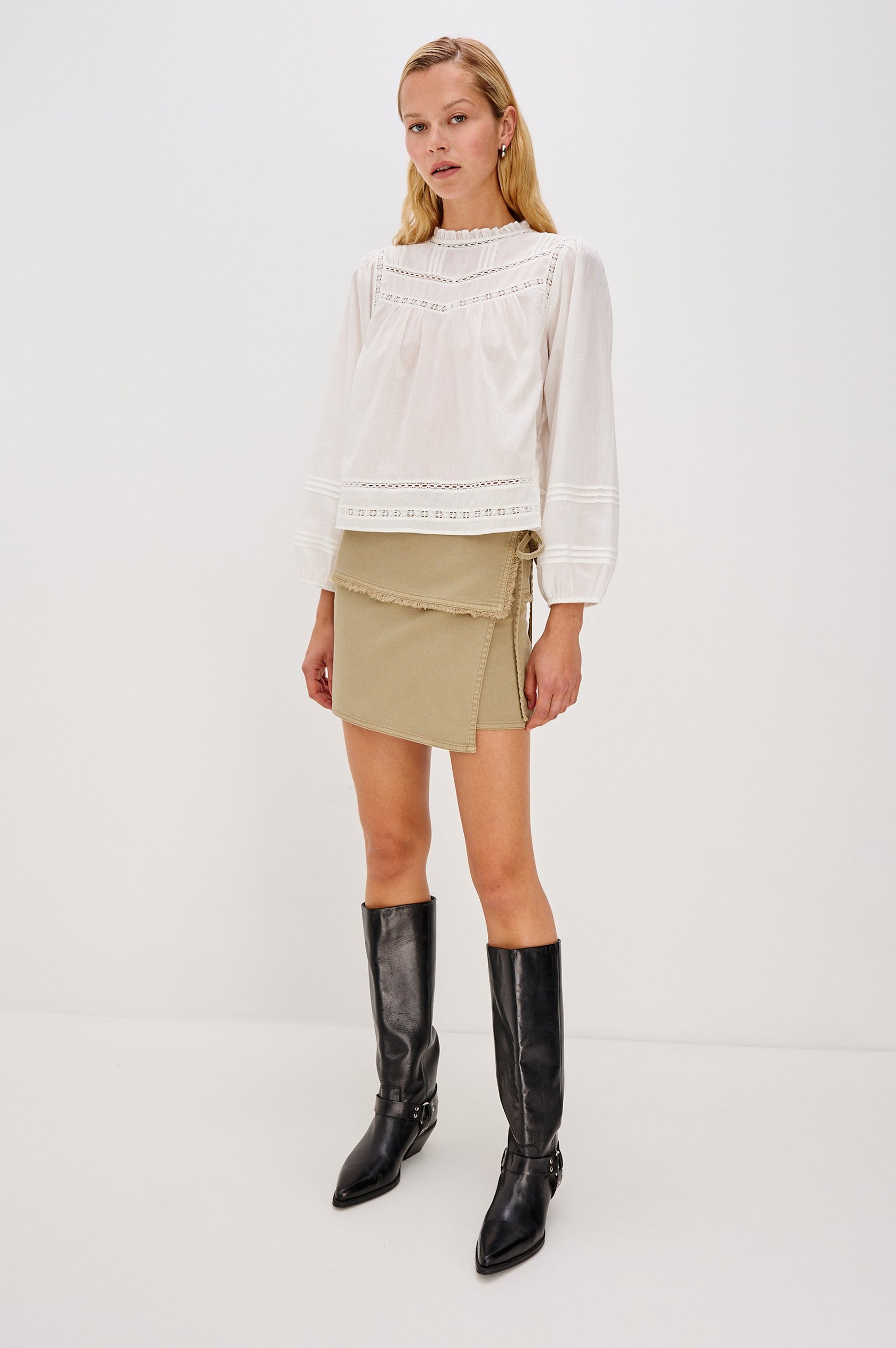 The Tamarin is a mini wrap front skirt with a tie side closure, it has a wide fold over waistband with a raw hem in Light Olive colorway. Front full body view featured on model