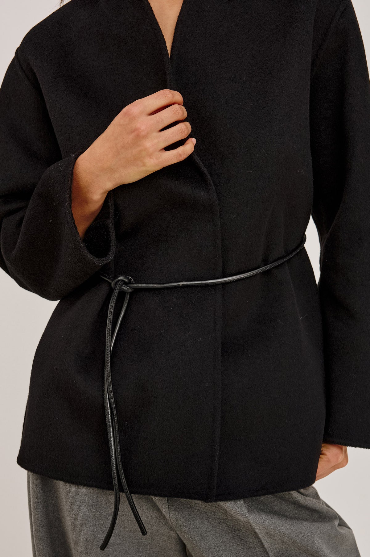 Tokyo Jacket in Wool Blend With Collarless Neckline, Leather Belt Ties, Long Sleeves, and Relaxed, Boxy Fit in Black Colorway - Upper Body Front Detail View Featured on Model.