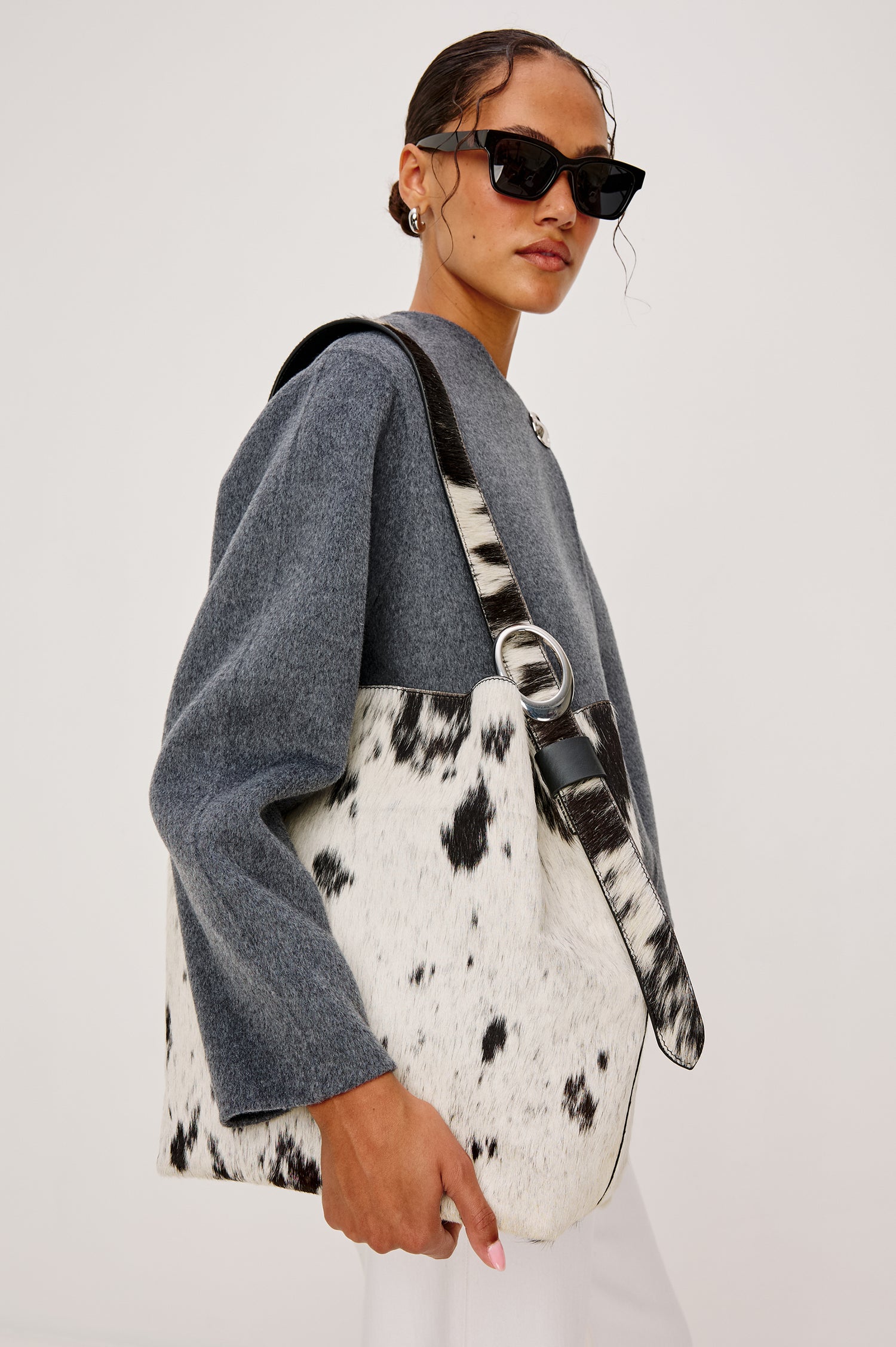 The Torino is a cow-print haircalf leather bucket bag, designed with an adjustable strap and polished silver oval buckle. Side view featured on model.