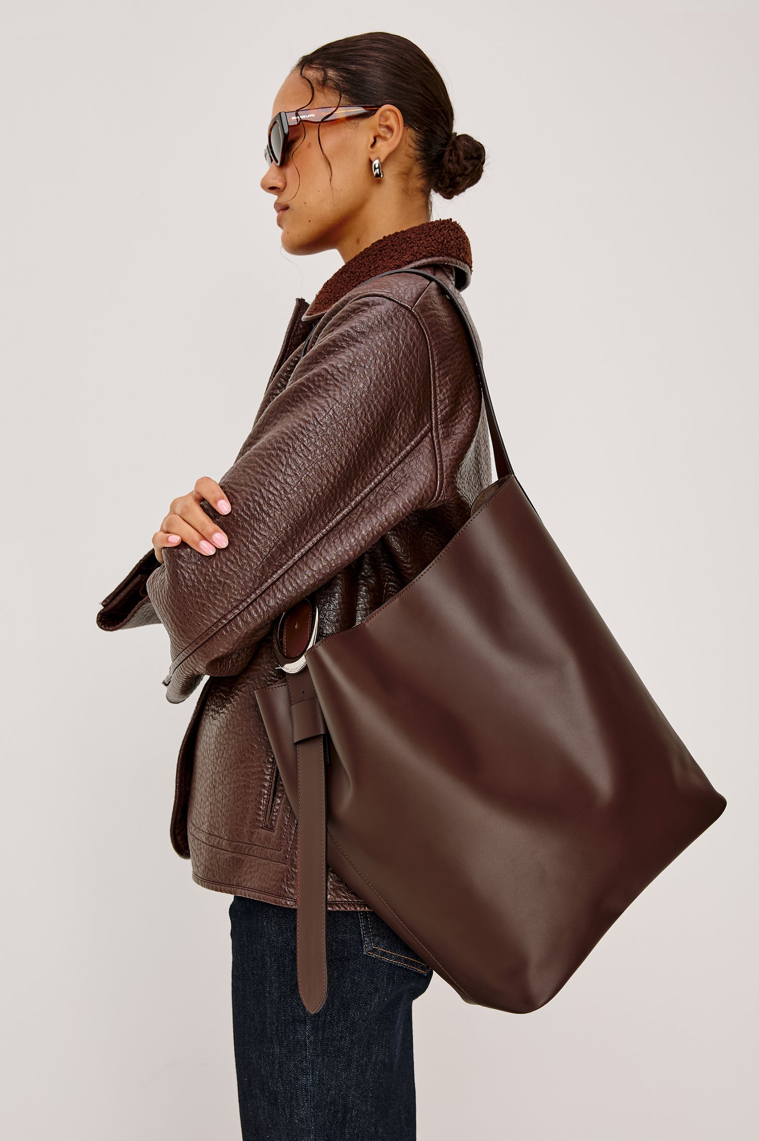 The Torino is a soft leather bucket bag, designed with an adjustable strap and polished silver oval buckle, in espresso colorway. Side view featured on model.