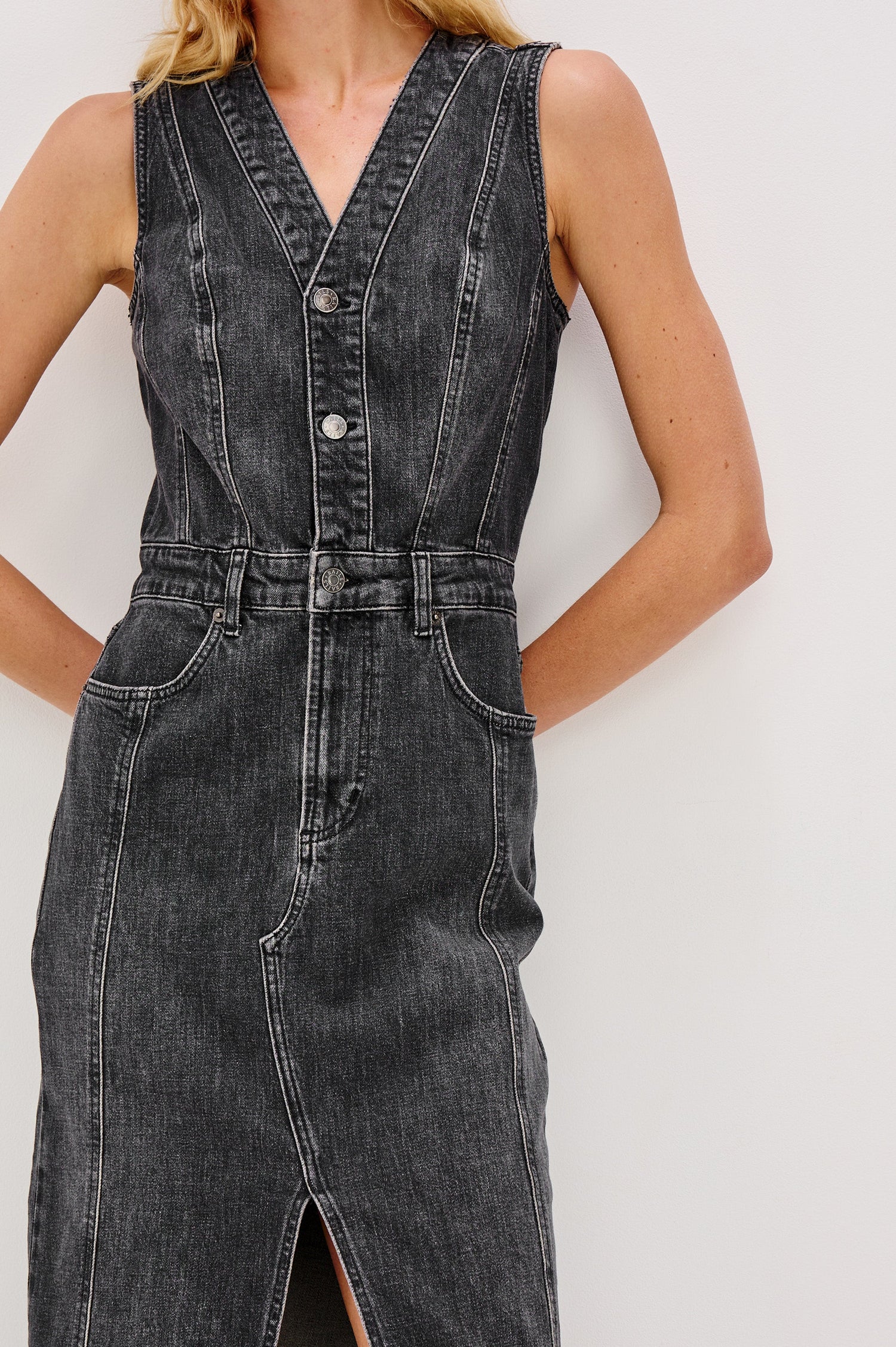 Westwood Sleeveless Denim Midi Dress with Belt Loops, a Button and Zipper Closure for the Skirt and Button Closure on the Bodice, a V neck, a Front Center Thigh Slit, Two Front Pockets  and Two Back Patch Pockets in Black Pearl Colorway, a washed black- Front Detail View Featured on Model