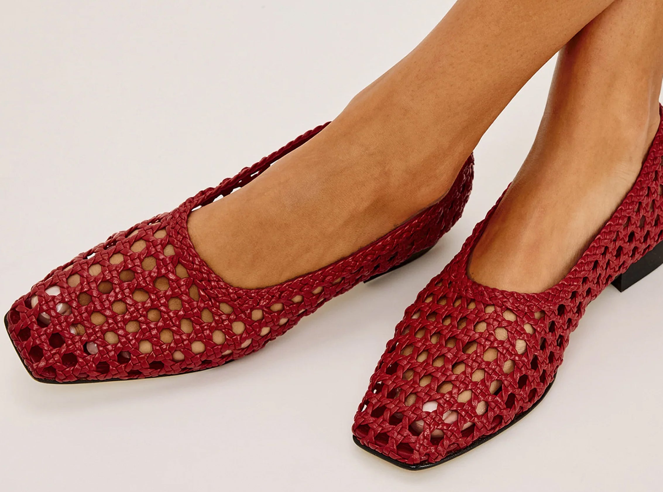 Red woven shoes worn by a person on a white background