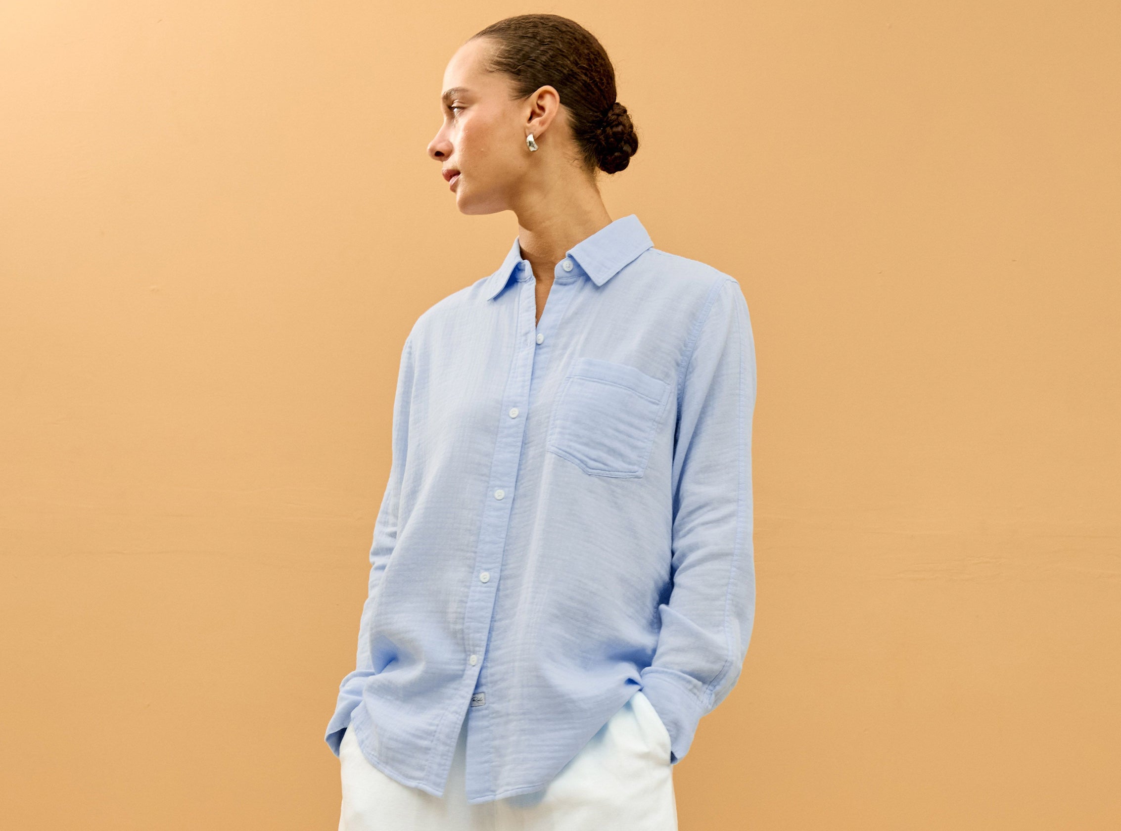 Woman wearing a light blue button-up shirt against a beige background