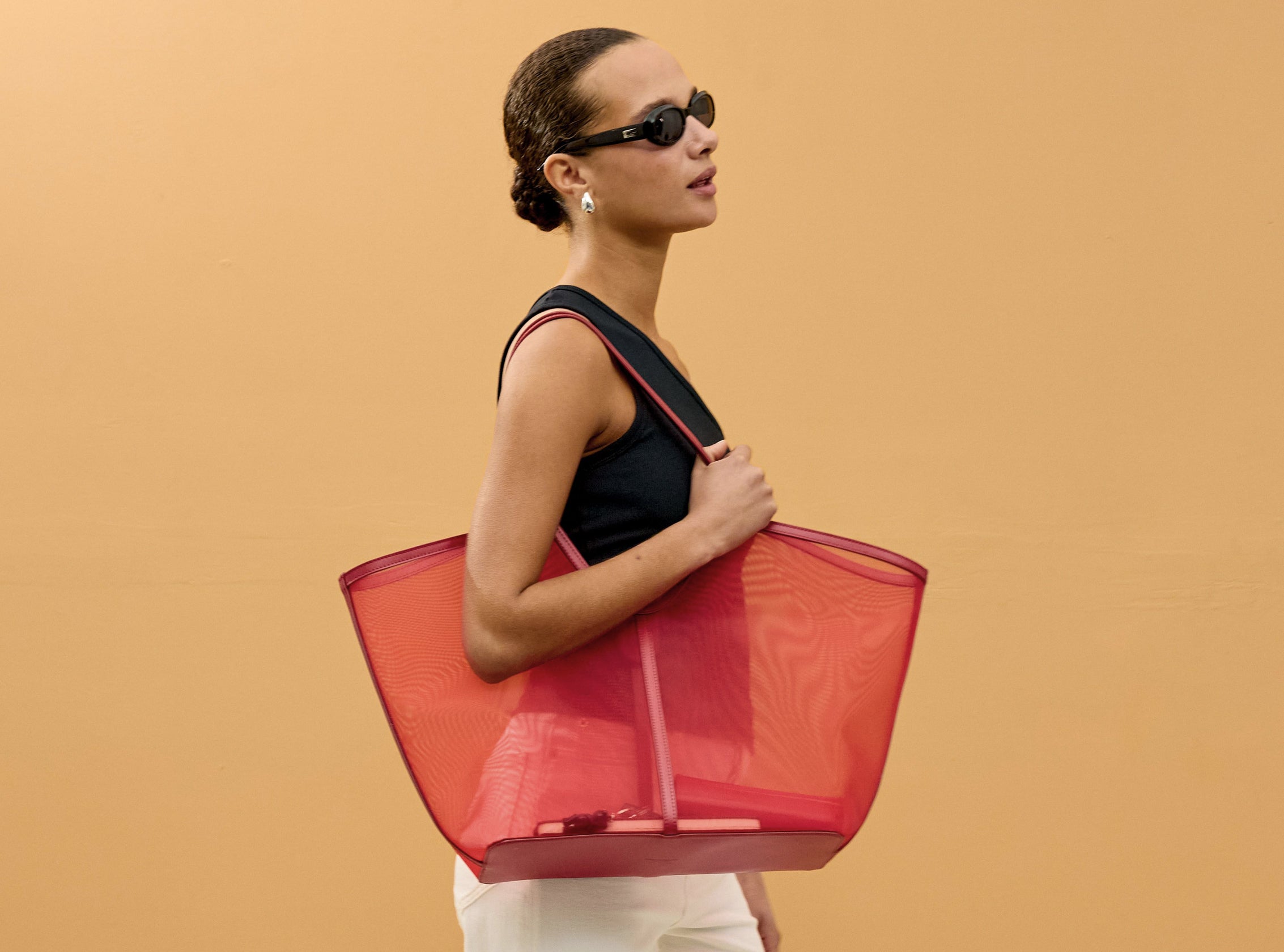 Woman holding a red transparent tote bag against a beige background