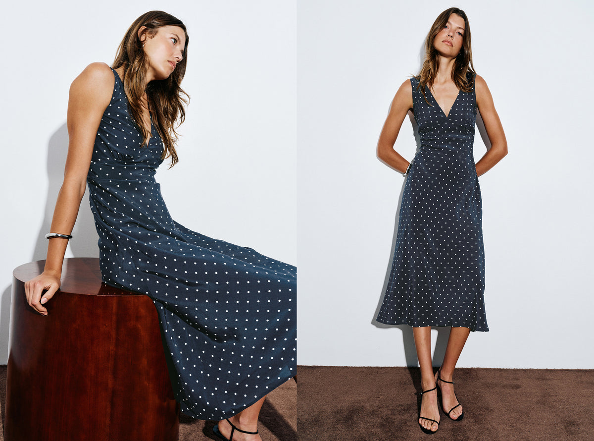 A sleeveless midi dress with a dark navy blue base and small white polka dots, shown on a model in two poses against a white studio background.