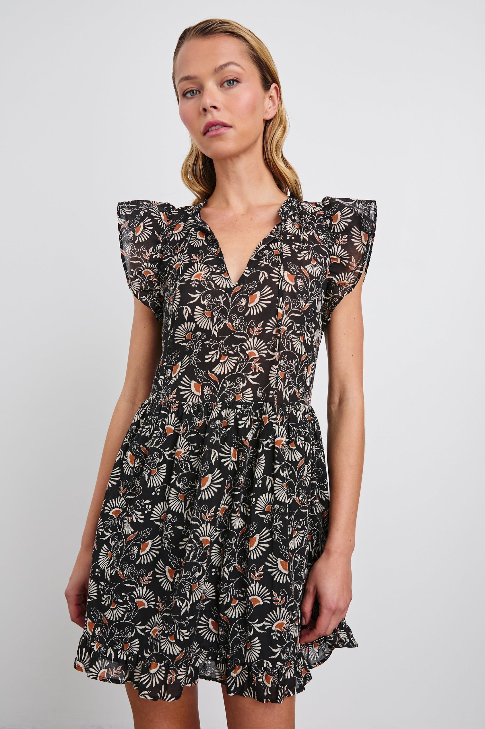 Zinnia Mini Dress with Flutter Cap Sleeves, and a Deep V Neck with Ties in Cassia Colorway, with Orange and Cream Flowers on Black - Front View Featured on Model 