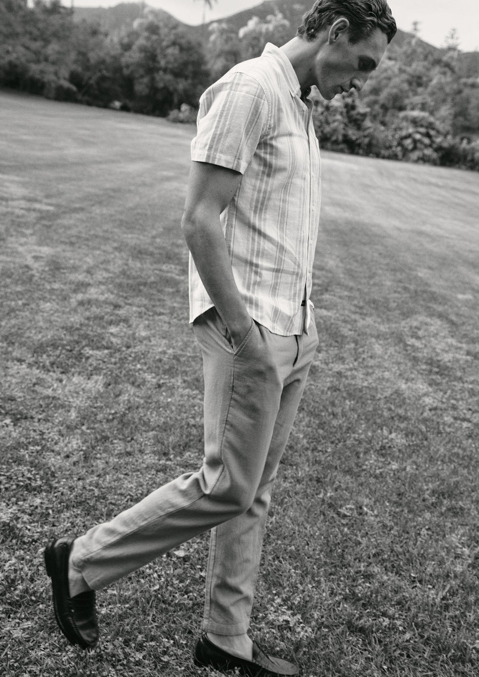 Man walking on grass wearing a striped shirt and light pants