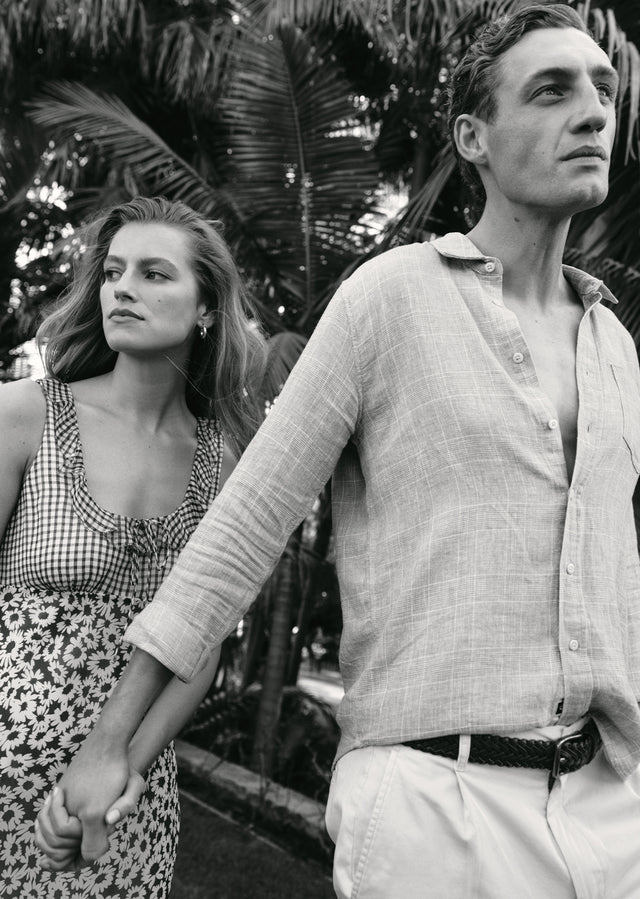Black and white photo of a man and woman holding hands outdoors with plants in the background