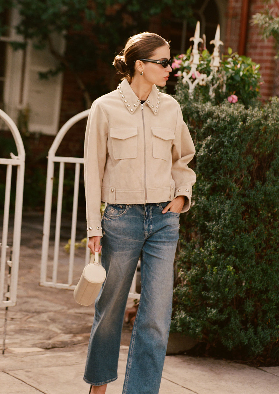 Woman wearing a beige jacket with studded details and blue jeans.
