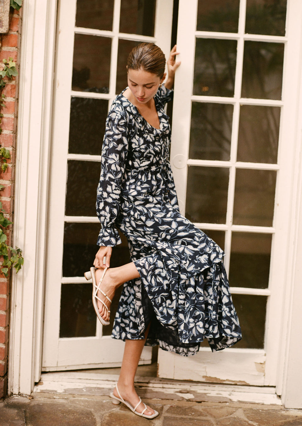 Woman in a floral dress standing in front of a white door.