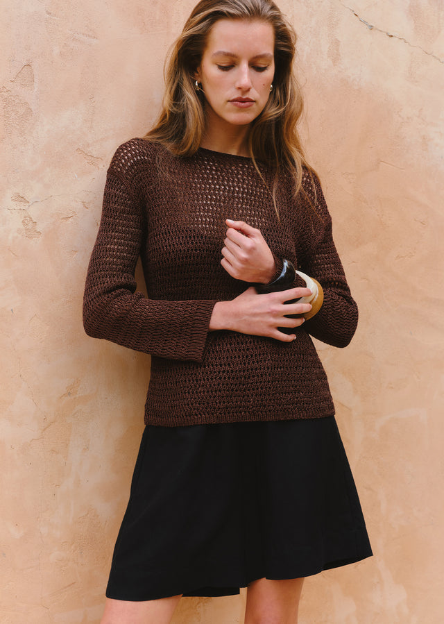 Woman wearing a brown knitted sweater and black skirt against a beige wall.