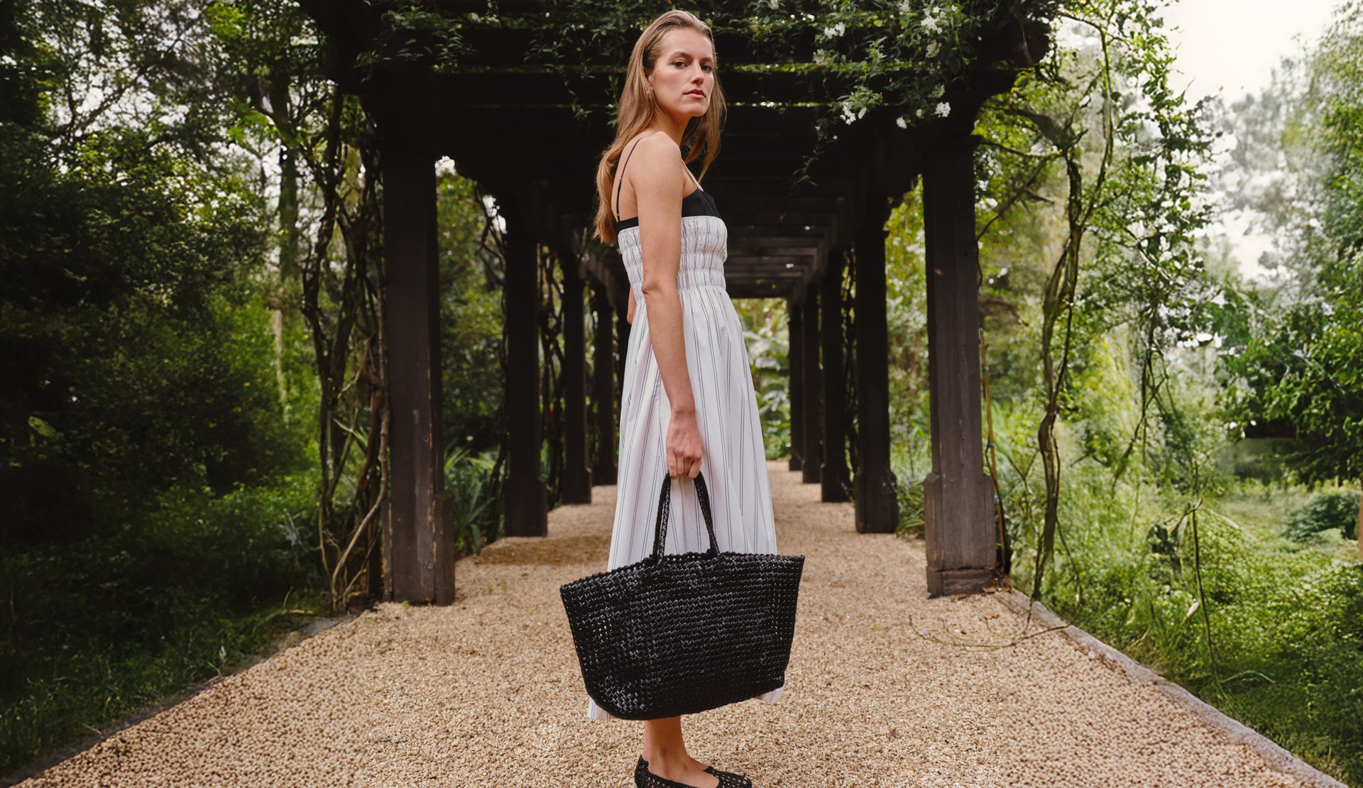 Woman in a white dress holding a black bag in a garden setting