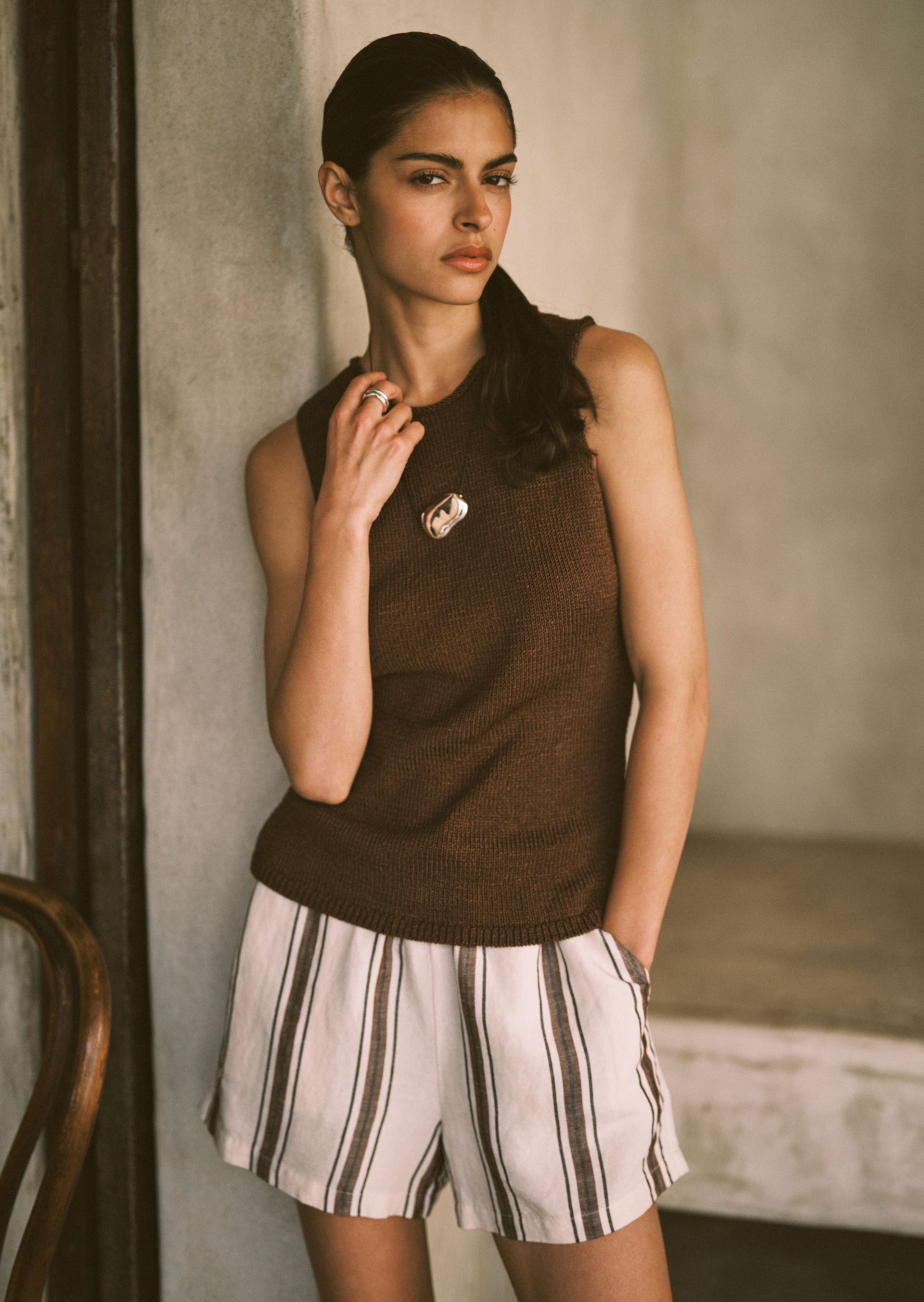 Woman wearing a brown sleeveless top and striped shorts in an indoor setting.