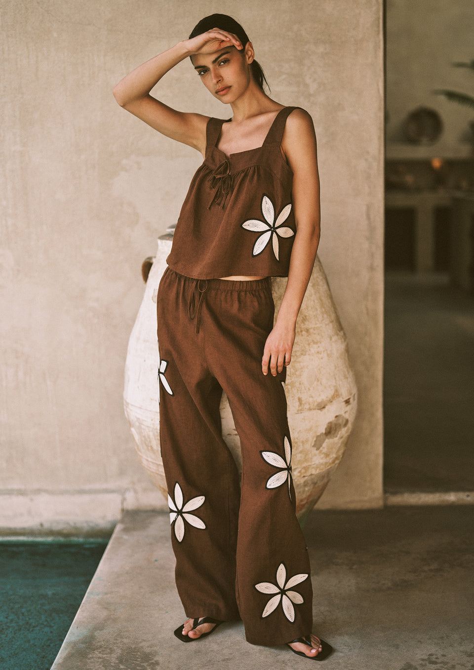 Woman wearing a brown outfit with white floral patterns standing by a poolside.