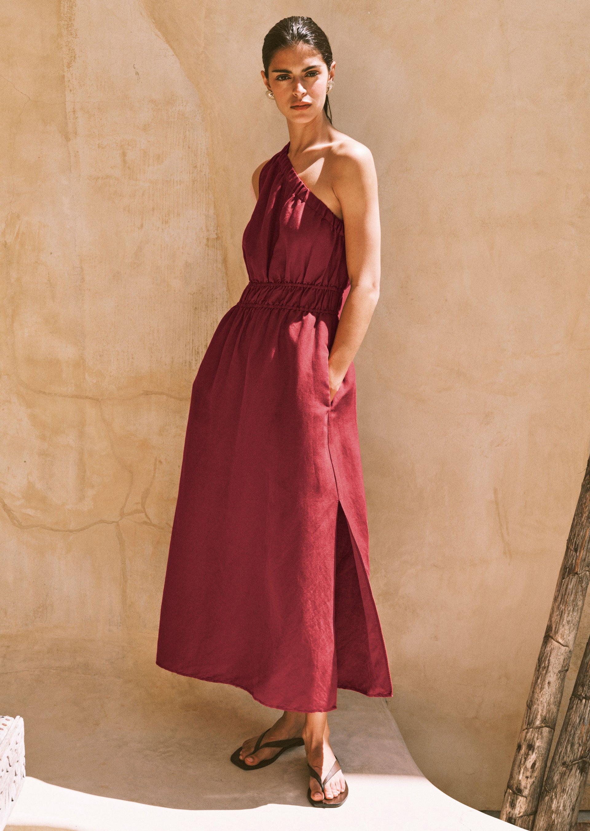 Woman wearing a burgundy dress against a beige wall.