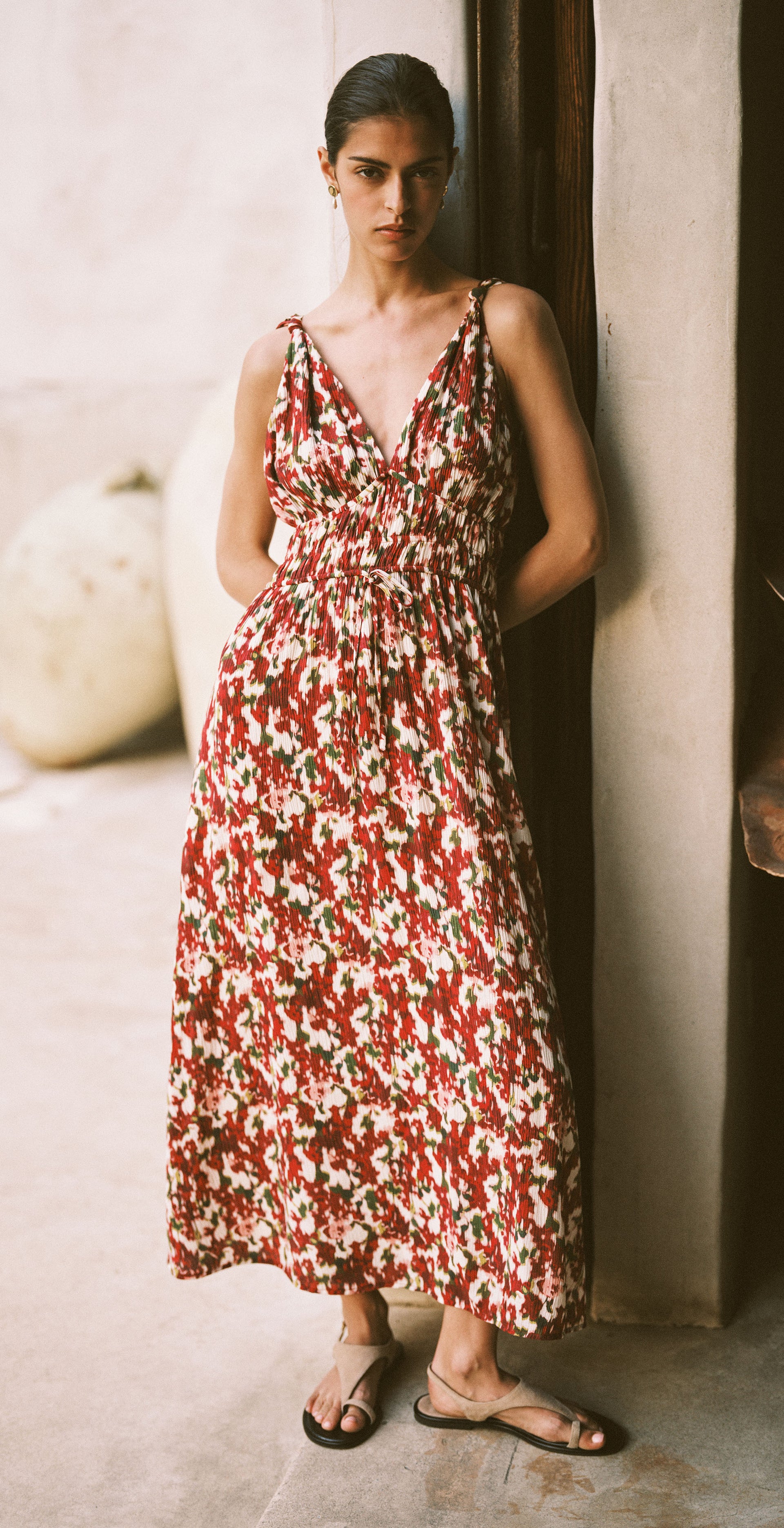 Woman wearing a floral dress leaning against a wall indoors.