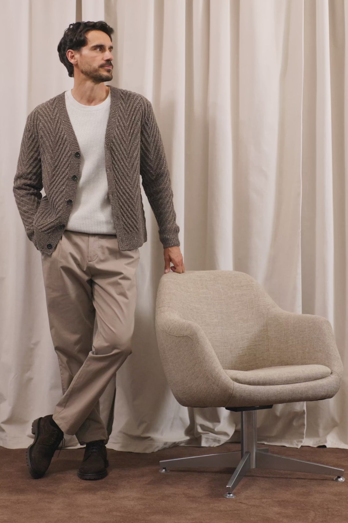 Adair Cardigan in Alpaca Wool Nylon Blend With Chevron Texture, V-Neck, Front Buttons, and Long Sleeves in Pine Log Colorway - Full Body View Featured on Model Posing with Chair (Video).
