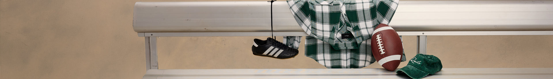 A horizontal banner-style graphic showing a beige wall and window trim with several sports items hanging from a hook: a black-and-white athletic shoe, a green-and-white plaid shirt, a brown football, and a green hat.