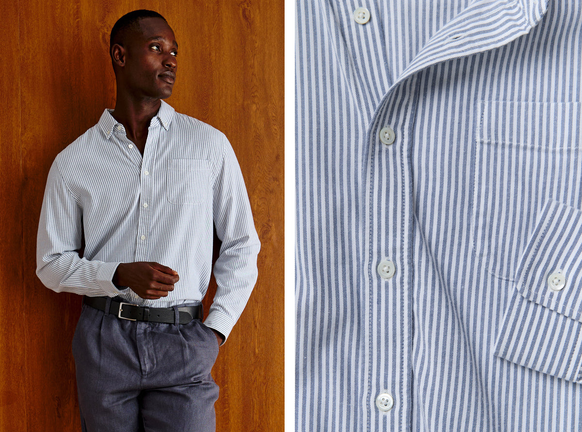 A man wearing a light blue and white vertically striped long-sleeve button-down shirt, paired with gray trousers and a black belt, standing against a warm wood-paneled wall. The right side of the image is a close-up detail of the shirt's striped fabric and buttons.